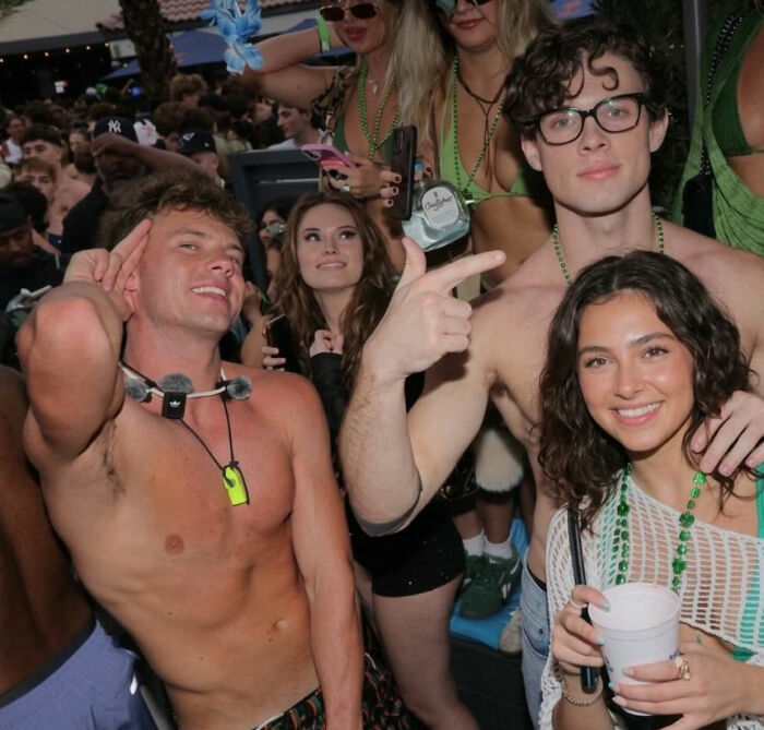 Group of young people partying at crowded event, looksmaxxer style seen with shirtless men and festive accessories