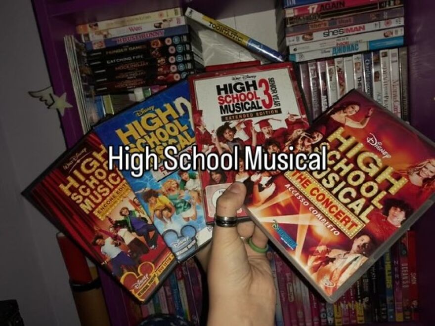A hand holds three High School Musical DVDs, a nostalgic photo capturing the vibe of growing up in the 2000s.