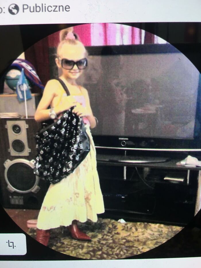 Child wearing oversized sunglasses and holding a large bag, posing in a funny and chaotic childhood photo indoors.