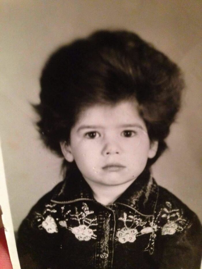Vintage chaotic childhood photo of a child with an exaggerated hairstyle and serious expression, capturing funny moments.