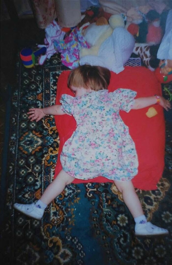 Toddler sprawled on floor surrounded by toys in a chaotic and funny childhood photo moment.