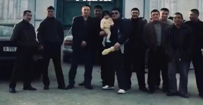 Group of men posing outdoors with one holding a child and a loaf of bread in a chaotic childhood photo moment