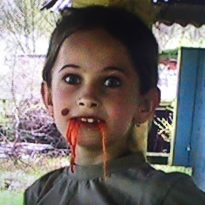 Child with messy face and red substance dripping from mouth in funny and chaotic childhood photo outdoors.