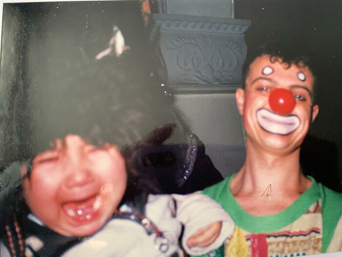 Child crying next to a person in chaotic childhood photo wearing clown makeup and a red nose.