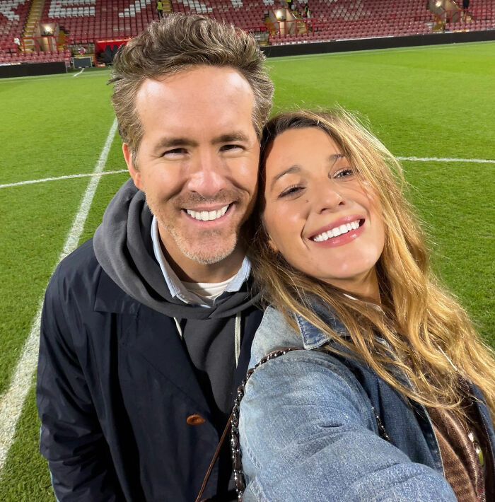 Couple smiling on a sports field with fans in the stands as many react explosively to Blake Lively lawsuit dismissal news.