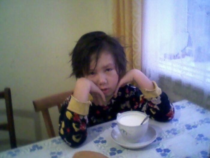 Child with messy hair sitting at a table with a cup of milk, showcasing a funny and chaotic childhood moment.