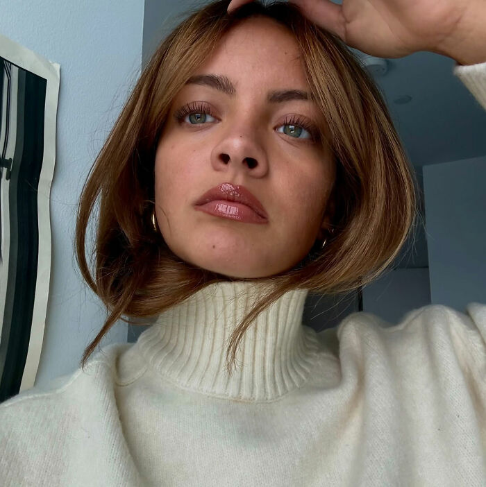 Young woman in a white turtleneck sweater posing indoors, illustrating a health and wellness girly after an airline incident.