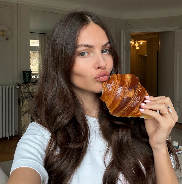 Coachella guest with long brown hair holding a croissant, showcasing beauty that turned heads at the festival.