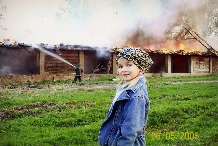 Smiling child in denim jacket and leopard headscarf with chaotic burning building and firefighter in the background.