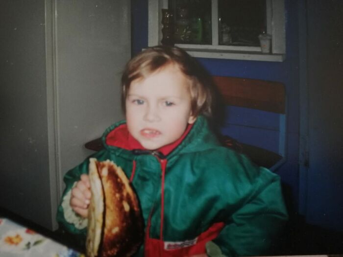 Childhood photo of a young child in a green jacket holding a burnt pancake, capturing a funny and chaotic moment.