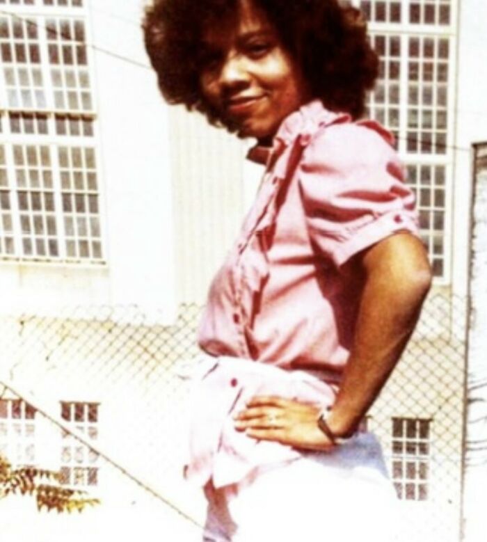 Woman with afro hairstyle wearing a pink blouse posing outside with a confident smile, illustrating stories about moms.