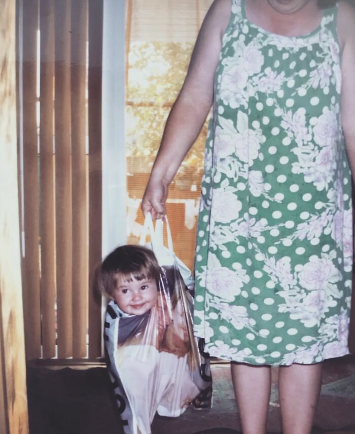 Childhood photo of a smiling child inside a plastic bag held by an adult in a floral dress, capturing a funny and chaotic moment.