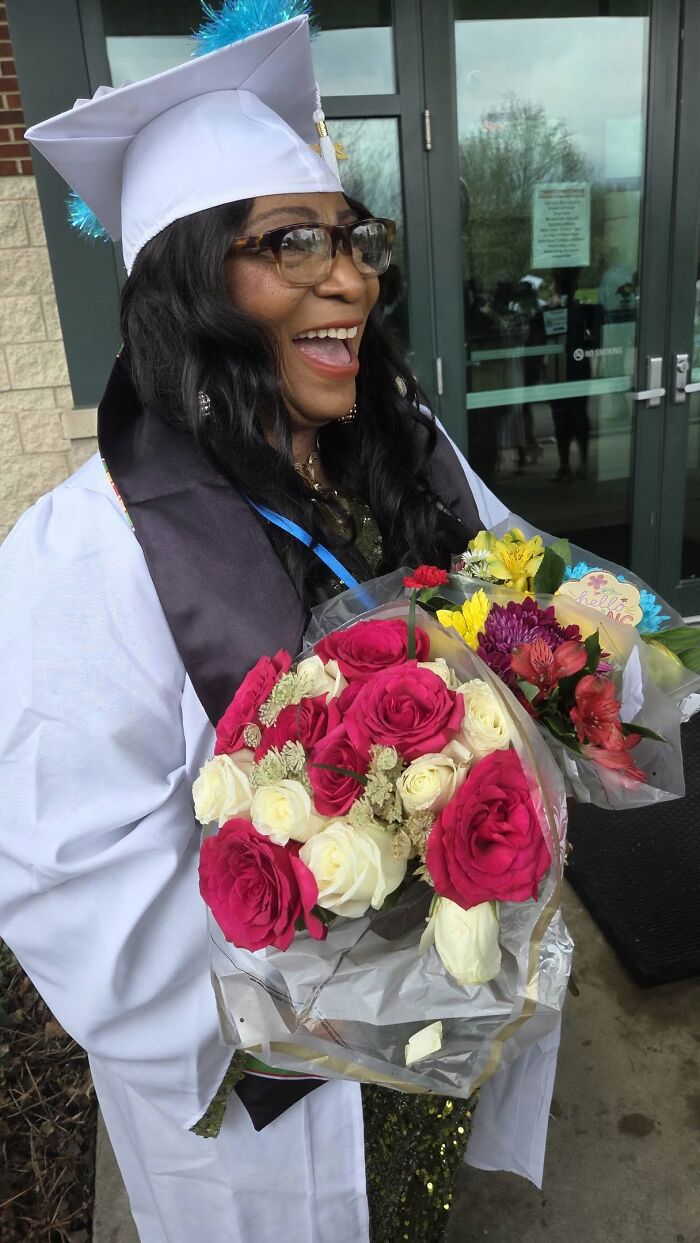 Smiling woman in graduation attire holding vibrant bouquets, celebrating an amazing story about their moms.