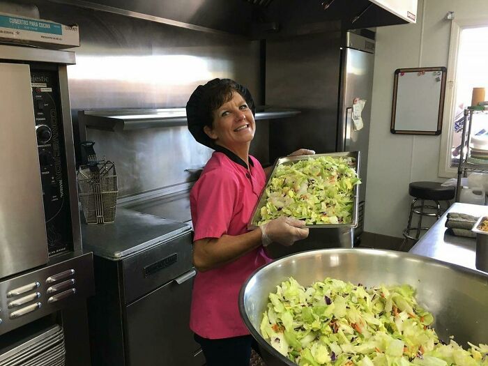 Woman preparing a large fresh salad in a commercial kitchen, sharing amazing and interesting stories about their moms.