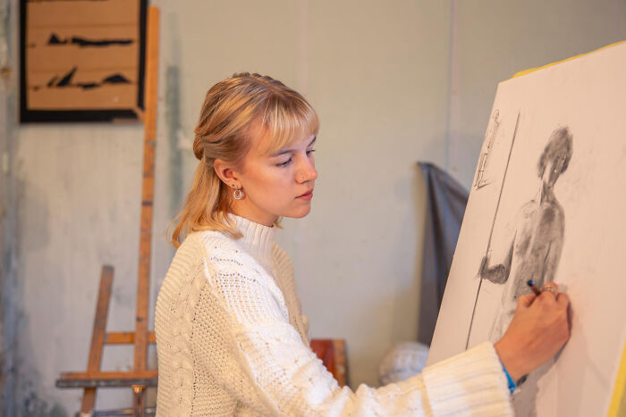 A young artist in a white sweater drawing a figure. This image makes one wonder about wildest rumors.
