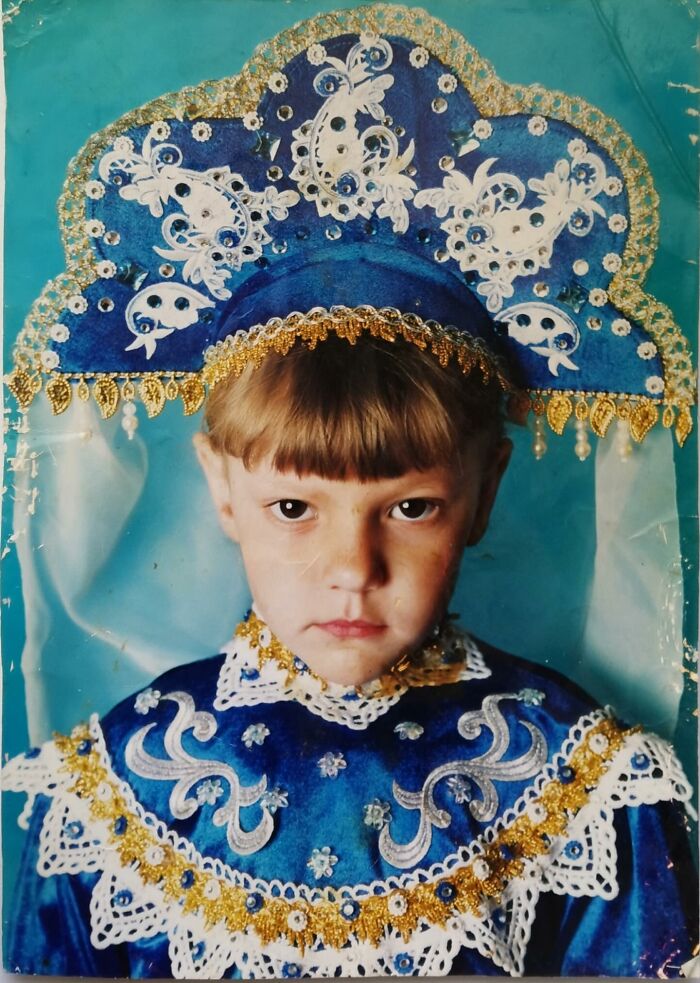 Child in chaotic childhood photo wearing an elaborate blue and gold traditional costume with serious expression