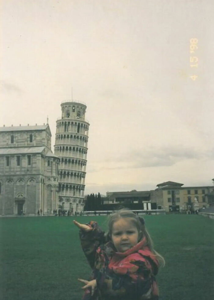 Child posing humorously in front of the Leaning Tower of Pisa in a funny chaotic childhood photo.