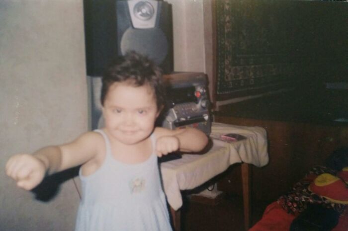 Child in a chaotic childhood photo making a playful fighting pose indoors with retro stereo equipment in the background.