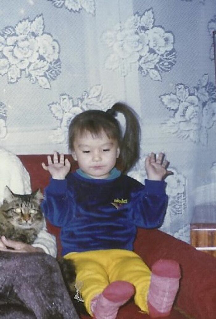 Child in colorful clothes sitting on a red couch with a cat, creating a funny and chaotic childhood photo moment.