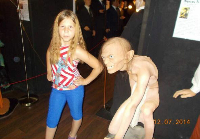 Young girl posing confidently next to a chaotic and funny childhood photo with an unusual creature figure.