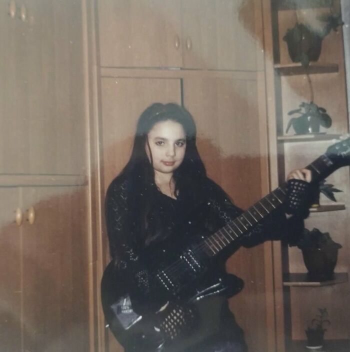 Young girl in dark clothing holding an electric guitar in a vintage chaotic childhood photo setting.