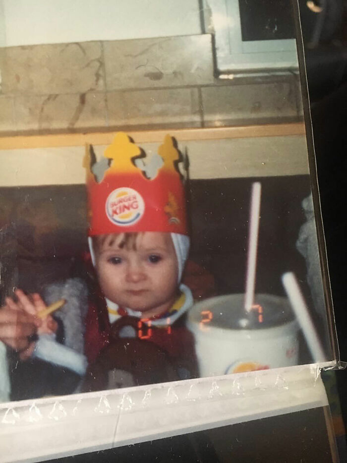 Child wearing Burger King crown and holding fries with a drink cup nearby in a funny and chaotic childhood photo.