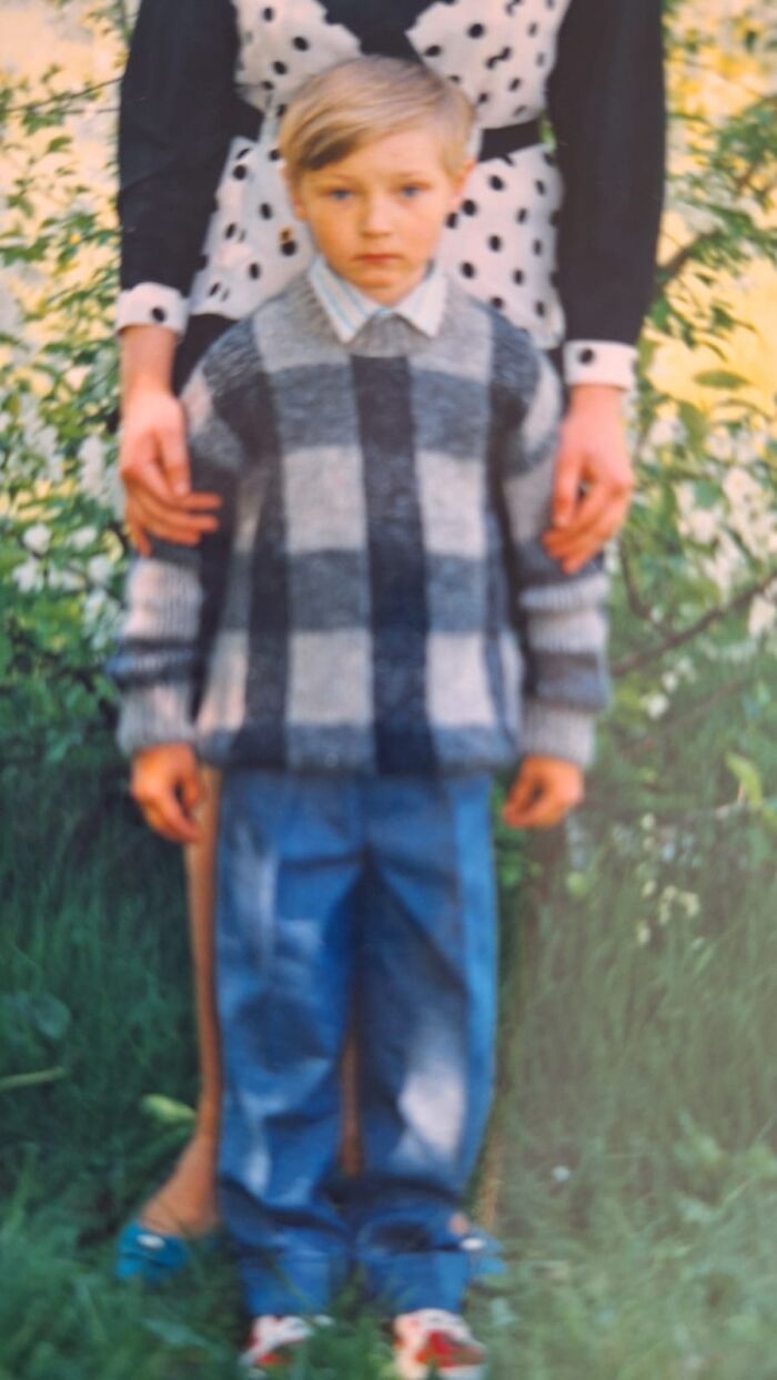 Blurred childhood photo of a young boy in a plaid sweater standing in front of an adult, capturing a funny and chaotic moment.