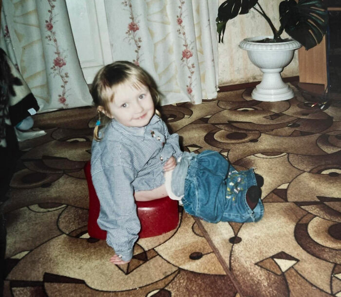 Child sitting awkwardly on a small red stool in a vintage room, one of the funny and chaotic childhood photos.