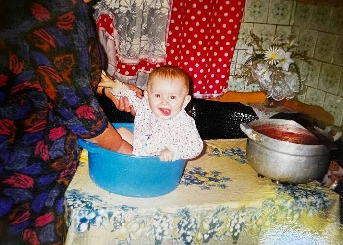 Baby sitting in a blue basin on a table with a colorful tablecloth, a funny and chaotic childhood photo moment.