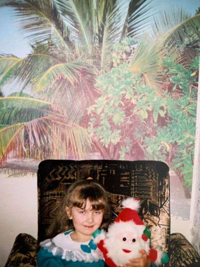 Young girl holding a Santa doll with a mischievous smile in a funny and chaotic childhood photo.