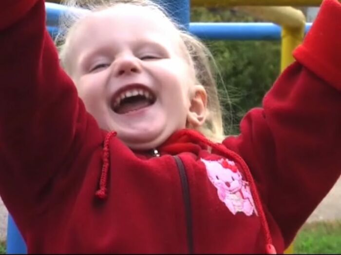 Young child laughing joyfully with arms raised in a playful and chaotic childhood moment outdoors.