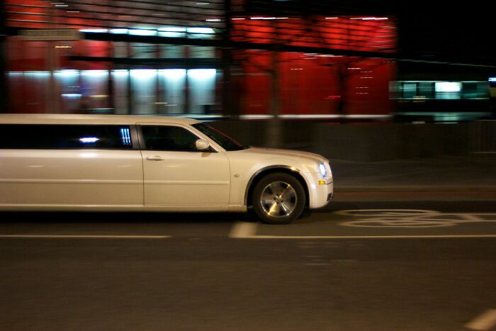 White stretch limo driving at night in an urban area, capturing the wild vibe of bachelor and bachelorette parties.