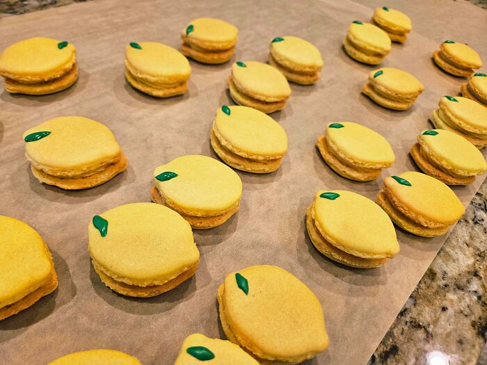 Yellow lemon-shaped macarons with green decoration on baking tray