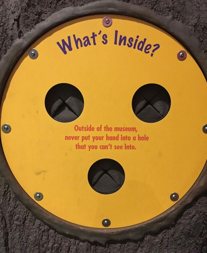 Yellow circular sign on a textured wall with advice about not putting your hand into unseen holes, reflecting funny pieces of advice.