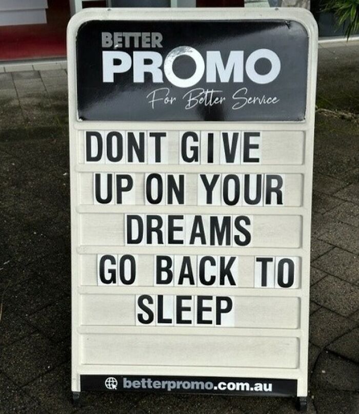 Funny pieces of advice on a sidewalk sign encouraging not to give up on dreams but to go back to sleep.