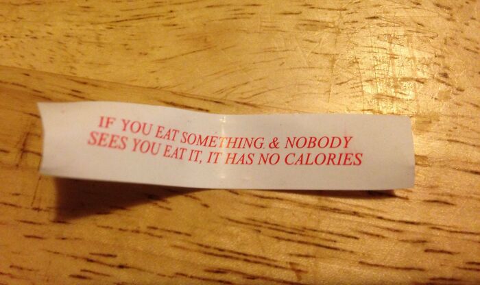 Fortune cookie slip on wooden table with funny pieces of advice about calories and eating habits.