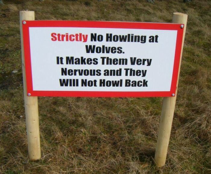 Funny advice sign warning against howling at wolves to avoid making them nervous in a grassy outdoor setting.
