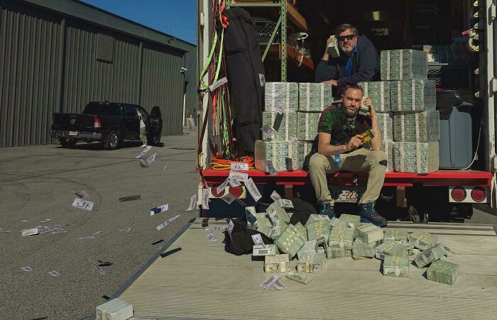Two men posing creatively on a truck full of money stacks with bills flying, showcasing hilarious and creative poses.