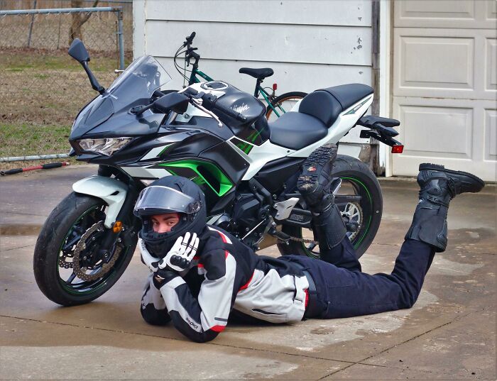 Person in full motorcycle gear lying on the ground in a creative pose next to a black and green sportbike.