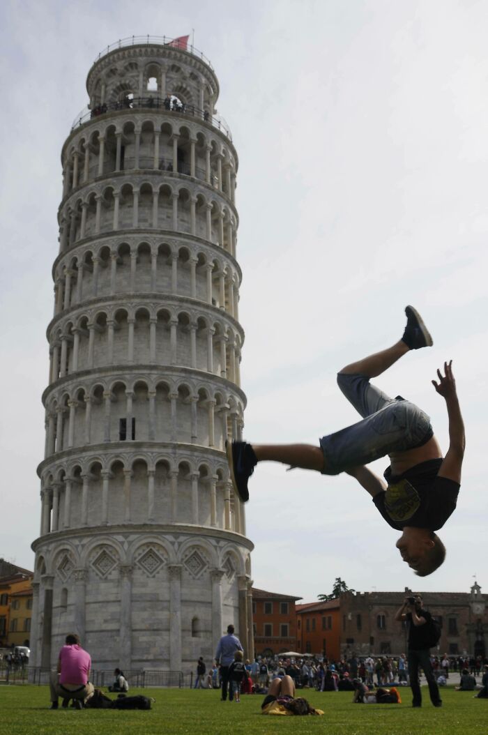 Person performing a creative pose mid-flip near the Leaning Tower of Pisa with a crowd in the background.