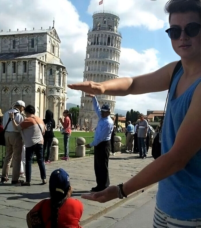 Tourists creatively posing to make it appear like they are holding up the Leaning Tower of Pisa in a humorous photo.
