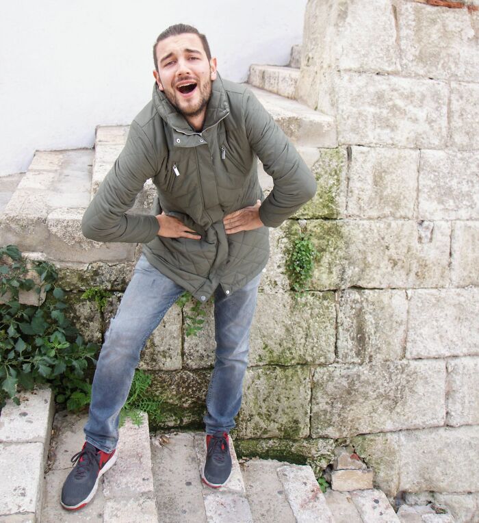 Man in green jacket pulling off a creative pose with a bent posture on stone steps, showcasing hilarious poses.