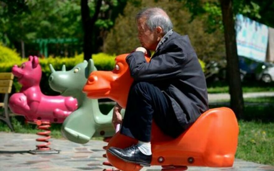 Elderly man enjoying playful moment on colorful playground ride, highlighting joy in learning interesting and fun facts.