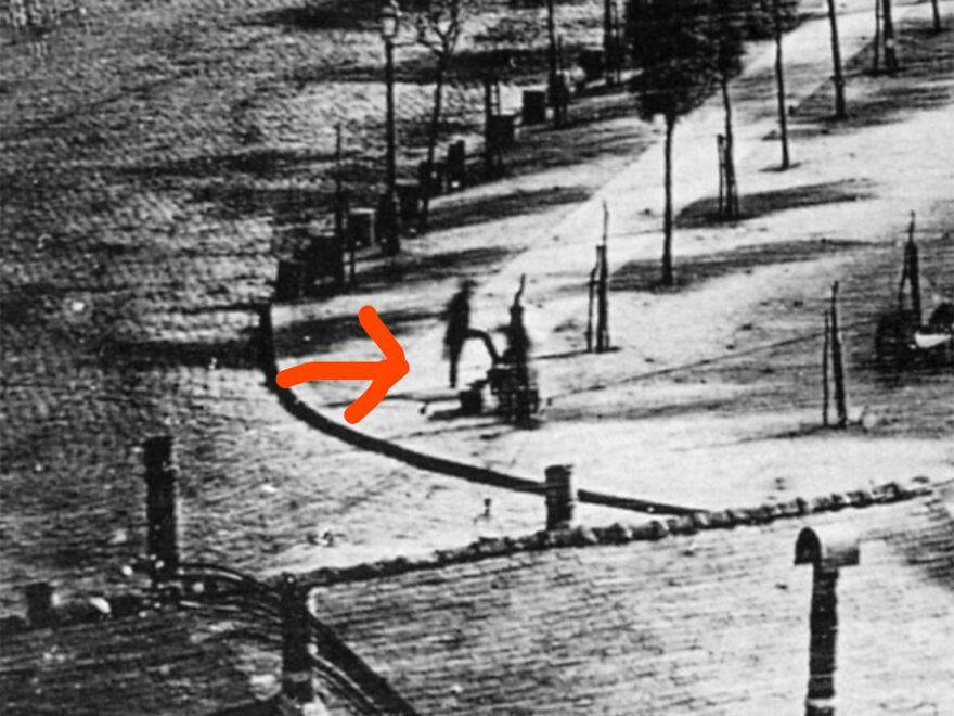 Black and white photo of a street scene with an orange arrow pointing to two blurred figures, illustrating fun facts about history.