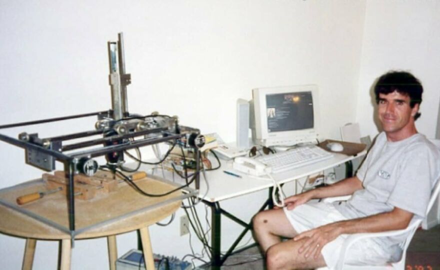 Man sitting next to a vintage computer and a homemade mechanical device, illustrating fun and interesting facts about technology.