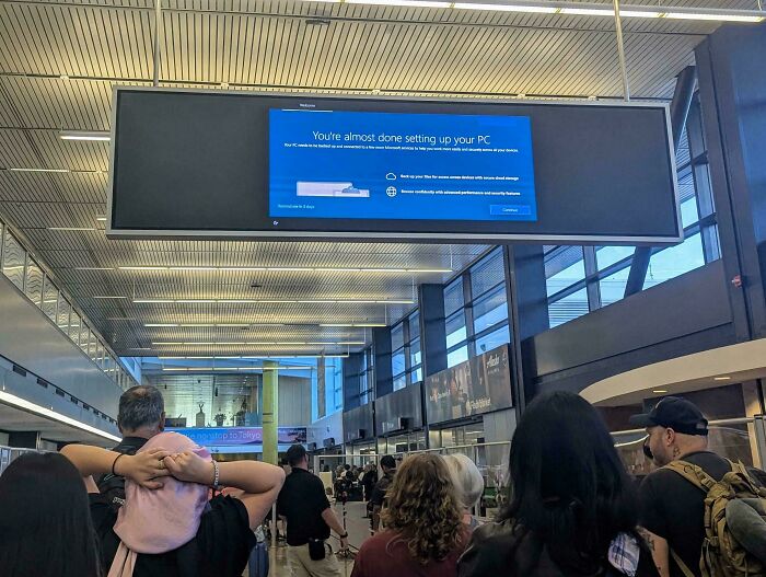 A large screen at an airport shows a Windows PC setup message, disrupting information flow in a chaotic place.