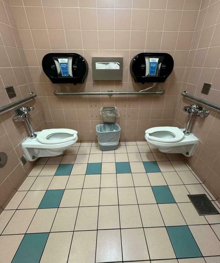 Two toilets are installed side-by-side in an airport bathroom, depicting a chaotic place.