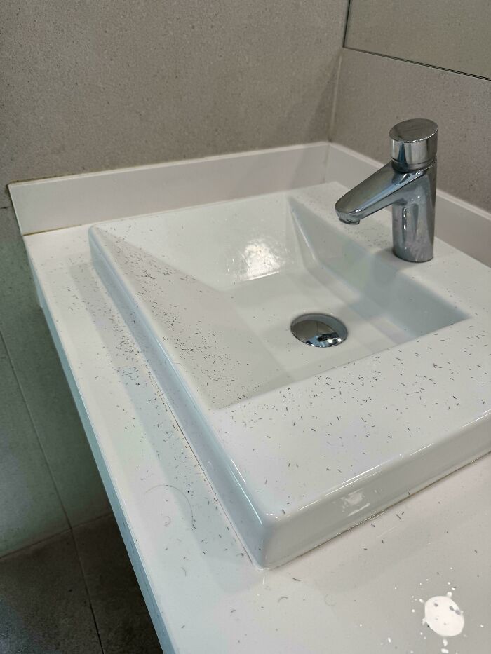 A dirty airport sink covered in hair clippings, revealing a chaotic place on the planet.