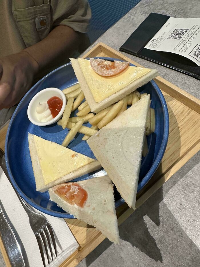 A plate of simple white bread sandwiches with cheese and a tomato slice, served with fries and ketchup, showcasing airport chaos.