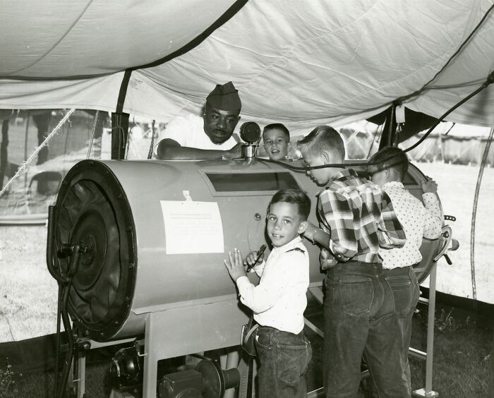 Vintage medical device demonstration with children and a nurse inside a tent, showcasing early healthcare technology.